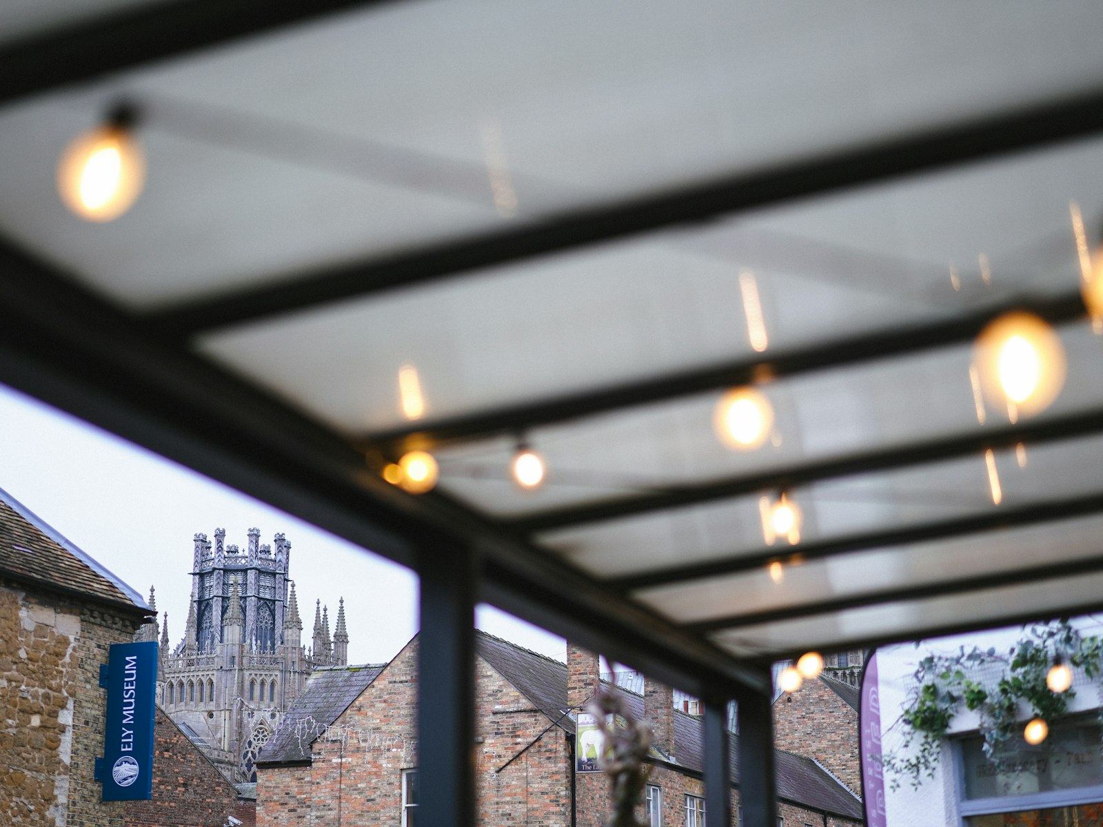 Glass canopy with hanging lights and a distant church tower.